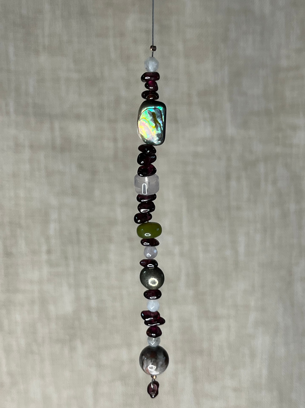 Beaded hanging ornament with multicolored natural crystal beads including garnets on a neutral background